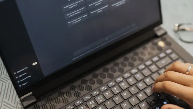 Hands typing on a laptop, an AI chat open on the screen