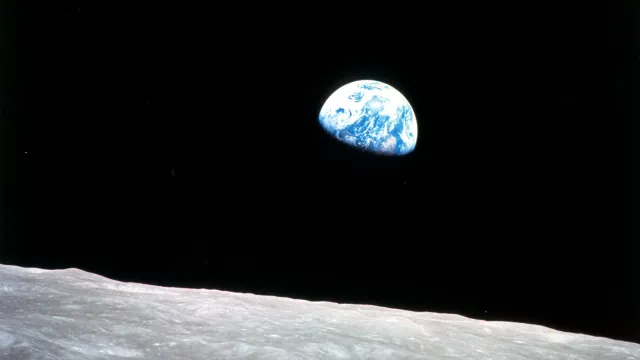 The Earth rising over the grey horizon of the Moon, half lit, against black space